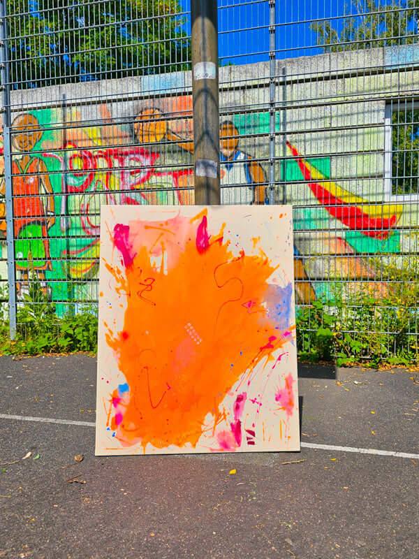 Farbintensive Neon Kunst mit leuchtendem Orange vor einer bunten Graffiti-Wand im Freien.