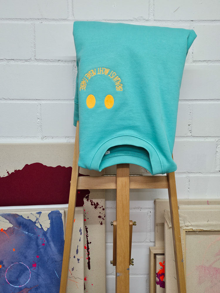 Sweater über eine Staffelei gelegt, Stickerei umgedreht sichtbar – kunstvoll inszenierte Slow Fashion.