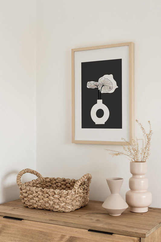 Minimalistischer Kunstdruck mit Blume in Vase auf dunklem Hintergrund, gerahmt über eine Kommode in einem Boho Schlafzimmer
