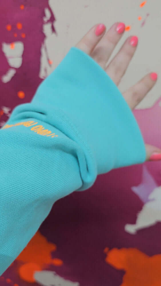 Ärmeldetail mit Stickerei „Studio Froilein Juno“, Hand mit pink lackierten Nägeln – individuelle Mode mit künstlerischem Touch.