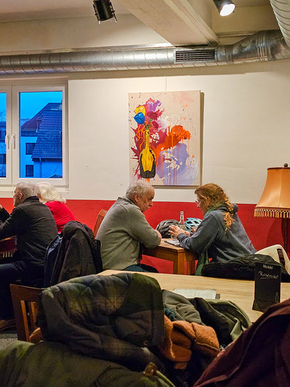 Gemälde „Flowers“ in einer belebten Bar in Bonn, Brotfabrik Bonn,  Gäste sitzen darunter, farbenstarkes abstraktes Blumenmotiv an der Wand.