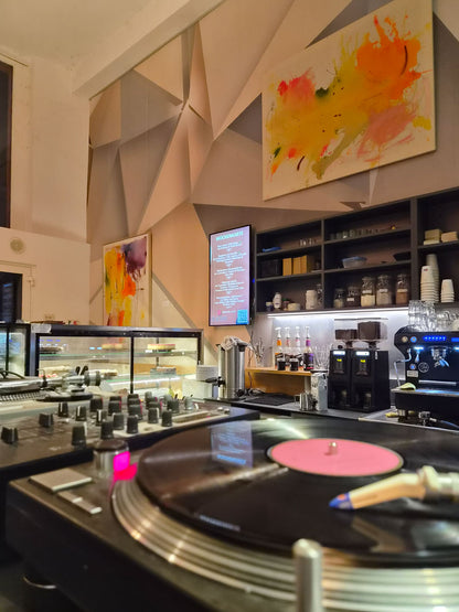 Abstraktes Gemälde „Colorful world no.1“ über der Bar eines Cafés, im Vordergrund ein Plattenspieler