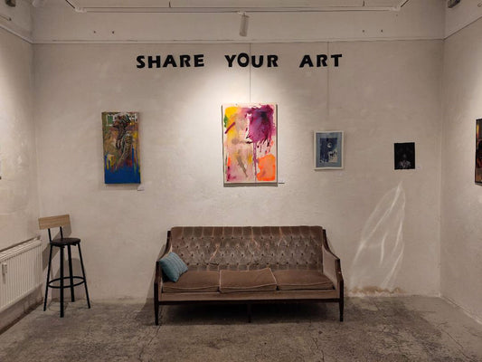 So sexy wie dus dir leicht machst no.1 in an exhibition: white wall with the words “Share your art”, a sofa in front